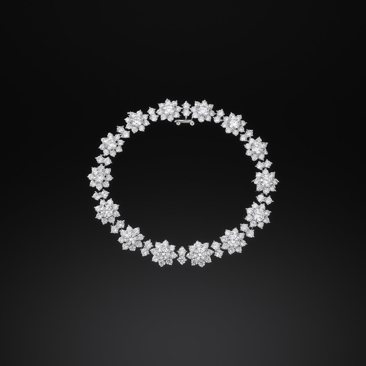 The Mossante Bloom Tennis Bracelet lying in a closed loop on a black ground: flowers of round stones, each a larger center ringed by eight petals, joined by two-stone links, every stone sharp.