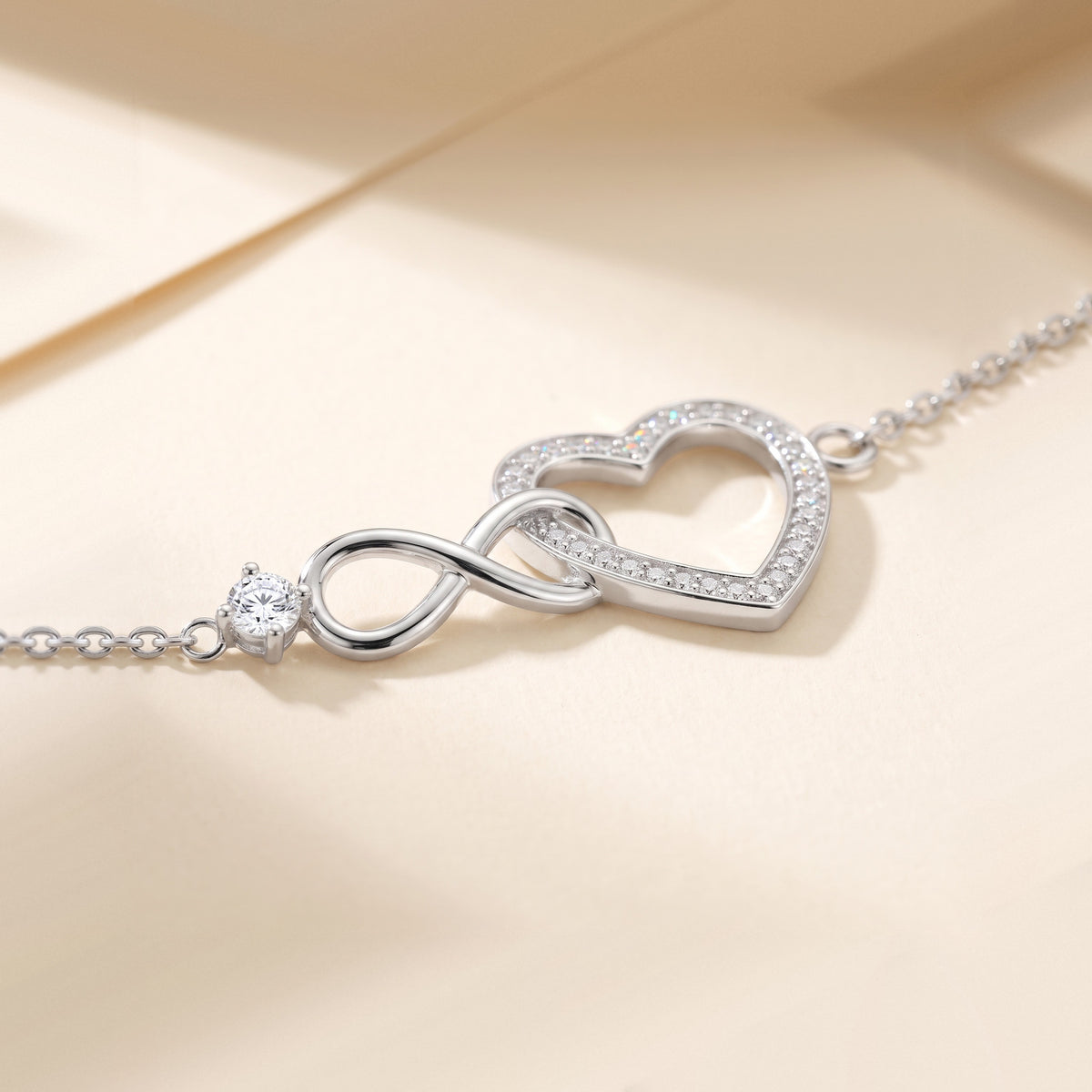Close view of the polished silver infinity passing through the side of the open heart, the row of small moissanites round the heart and the round stone in its prongs, light breaking into color at the facets.