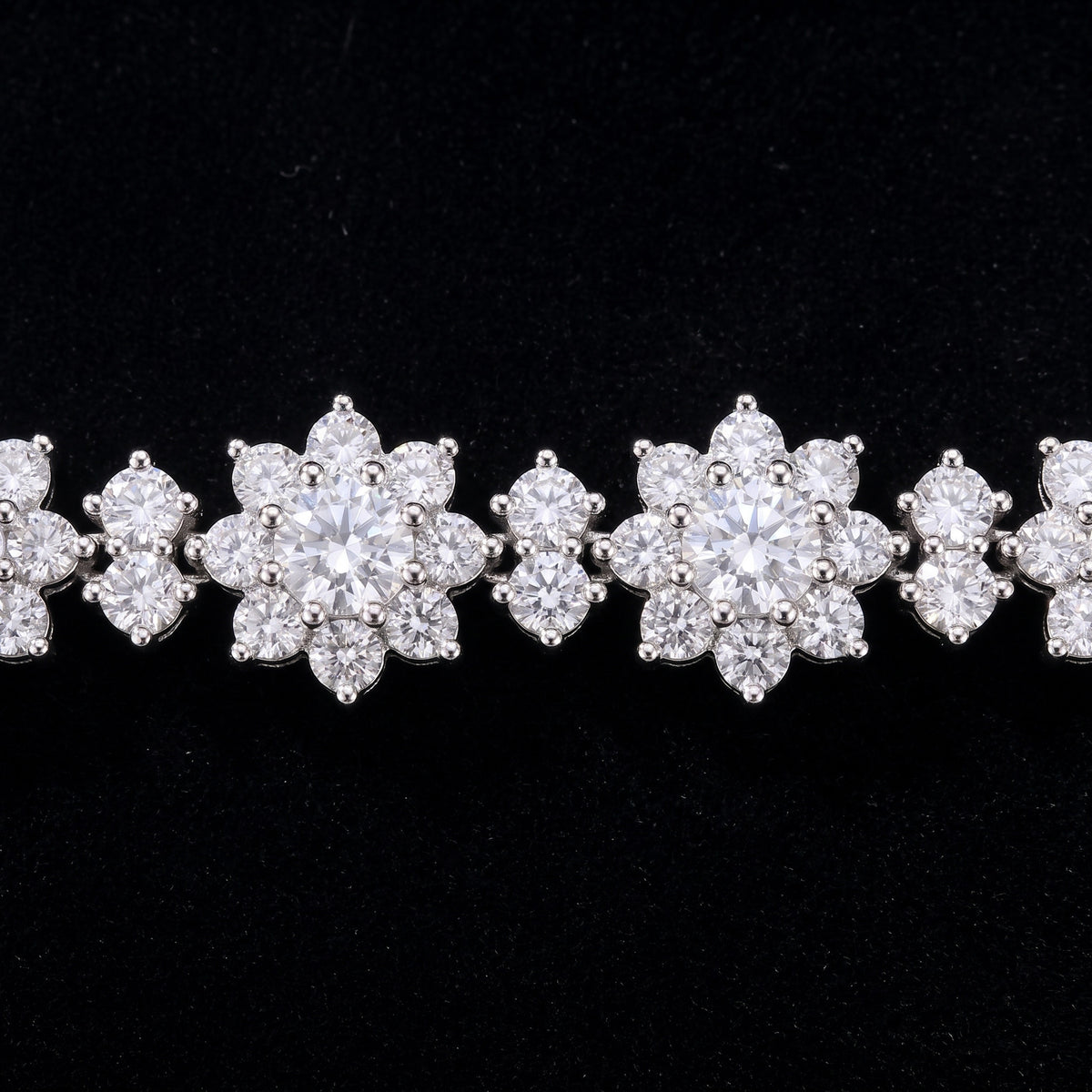 Close view of two flowers and the two-stone link between them on a black ground: in each flower a larger round center stone ringed by eight round petals, every stone held in small claws of bright white metal.