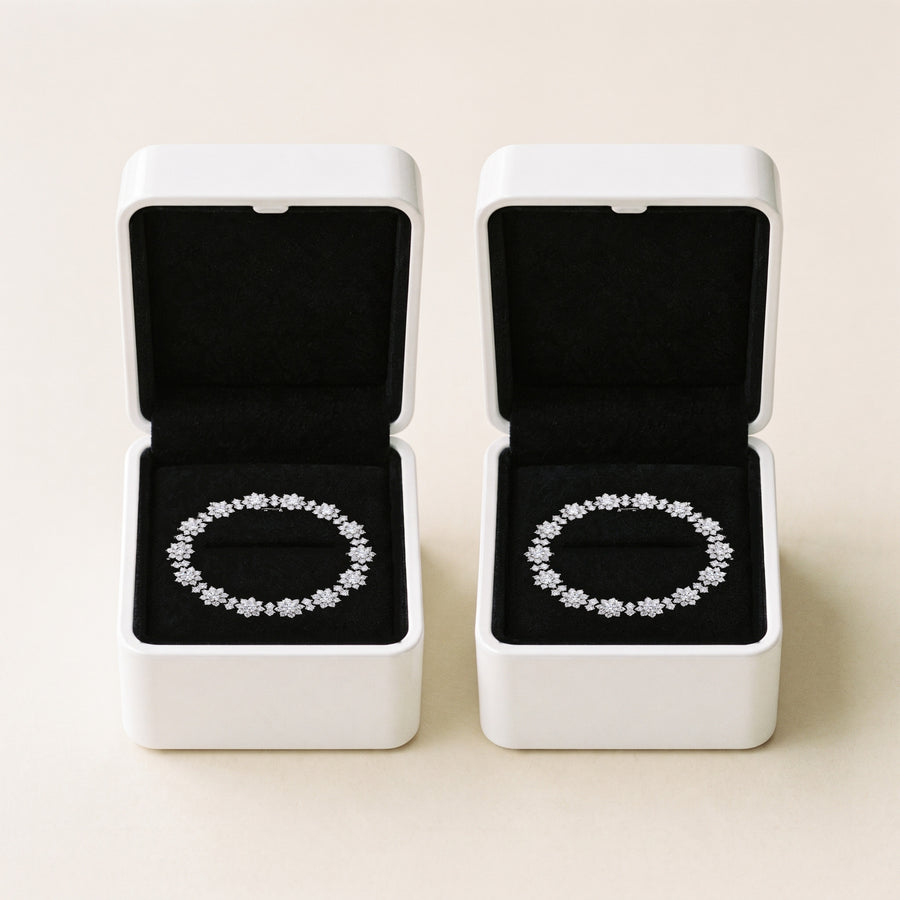 Two open white boxes side by side on a cream ground, black velvet inside each, a silver Bloom tennis bracelet lying in each box.