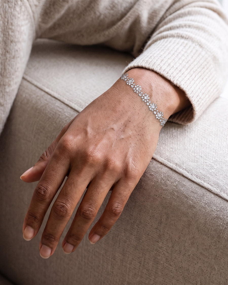 A woman's hand resting on the arm of a linen sofa, a cream knit sleeve pushed back, the silver Bloom tennis bracelet a fine sparkling line around her wrist.
