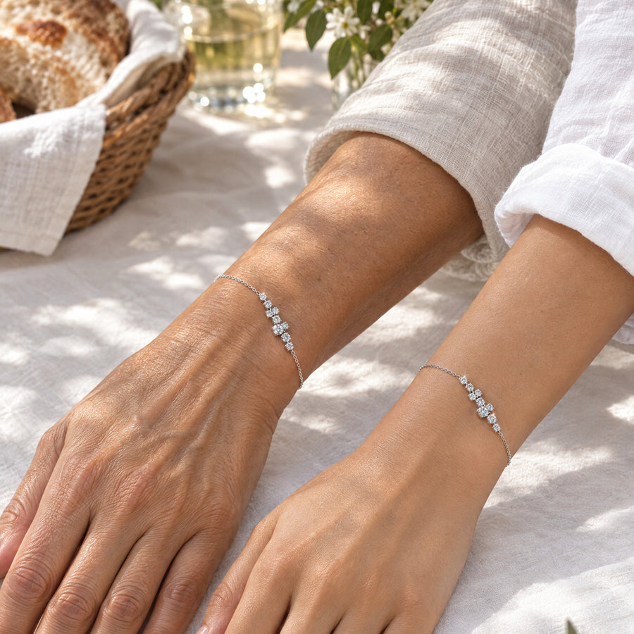 Two women's wrists side by side on white linen at a garden lunch, each wearing the constellation bracelet.