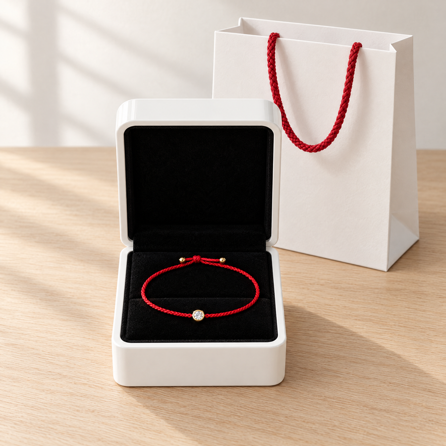 A red Mossante cord bracelet in its open white box lined in black velvet, the gift bag beside it