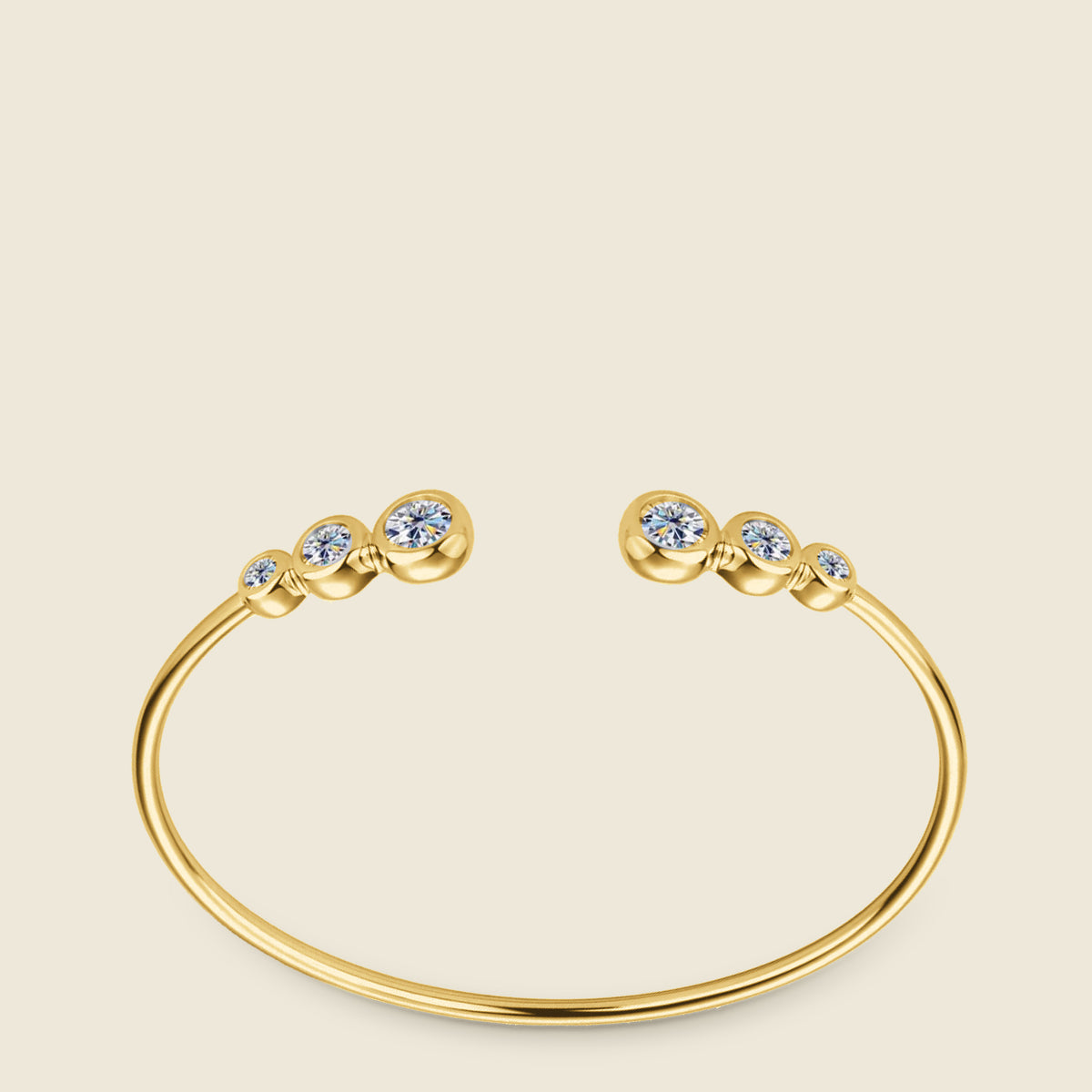The gold plated cuff on a cream ground, turned so its opening runs across the center: at each end three round moissanites in smooth rounded bezels with small ridged collars between them, the two largest stones at the tips facing each other across the gap, light breaking into color at the facets.