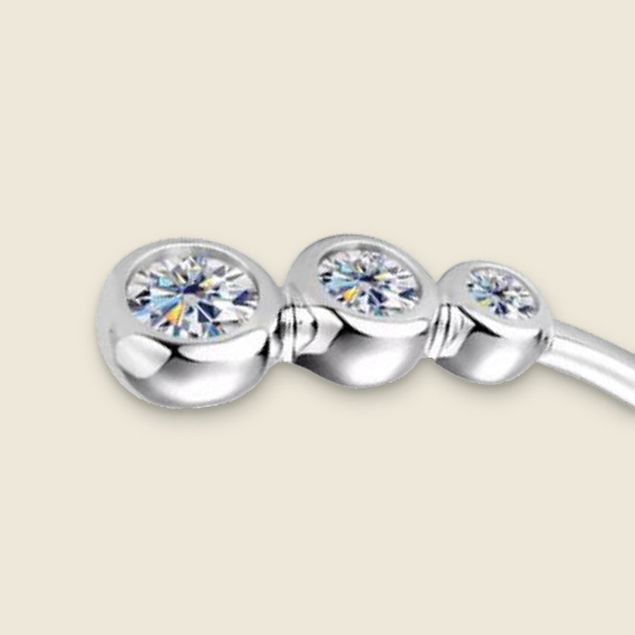Close view of one end of the silver cuff on a cream ground: three round moissanites stepping down in size from the tip, each closed in a smooth rounded bezel, small ridged collars between them, the wire running on from the smallest.