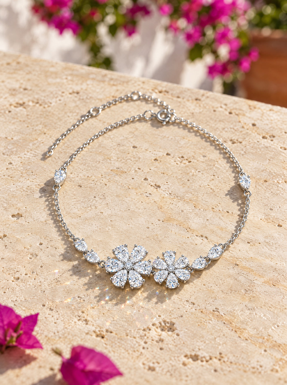 The Mossante Floral Bracelet laid on a sunlit travertine ledge, bougainvillea behind: two six-petal flowers of pear-cut moissanite at the center of a fine sterling silver chain, a pear station on each side.