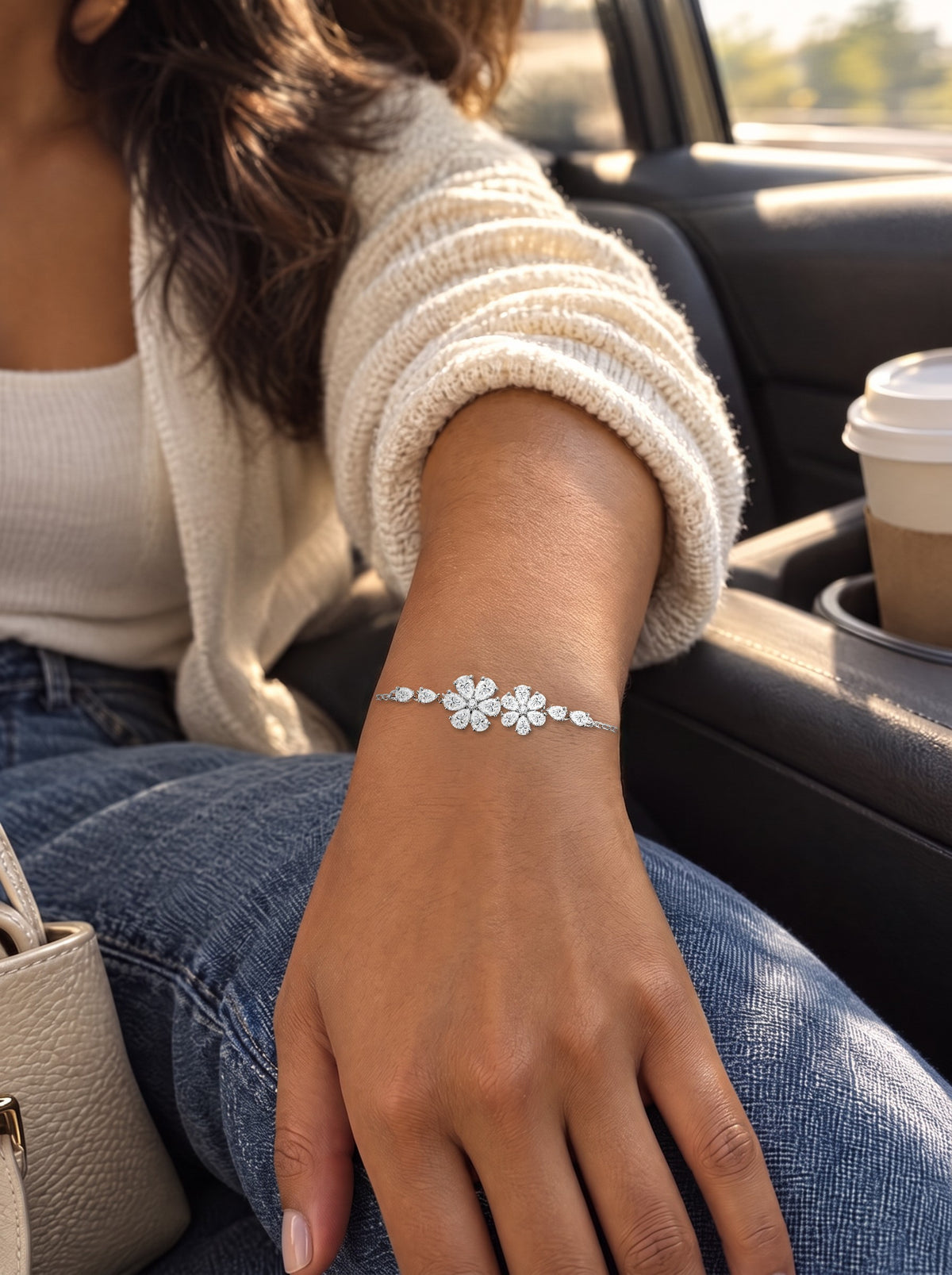 The bracelet worn on a wrist resting on a denim knee in the passenger seat of a car, afternoon light through the window, a coffee in the cup holder.