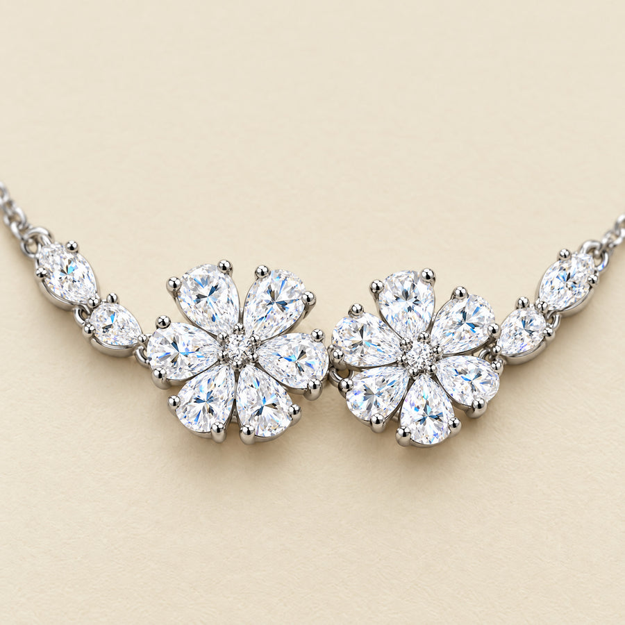 Close view of the two prong-set six-petal flowers, each petal a pear-cut moissanite around a small round center stone.