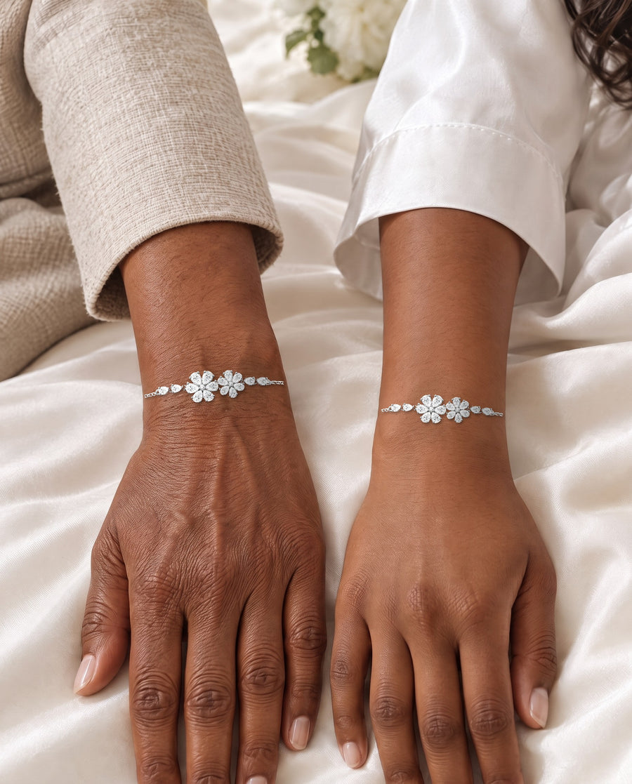 A mother's and a daughter's hands resting side by side on the ivory satin of a wedding dress on the morning of the wedding, each wrist wearing the floral bracelet.