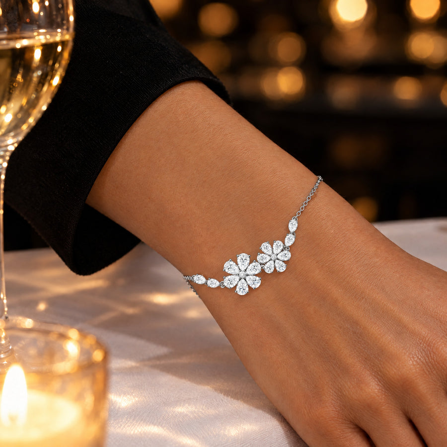 A woman's wrist on a dinner table in candlelight, a glass of white wine and a tealight beside her, the pear-cut stones flashing in the low light.