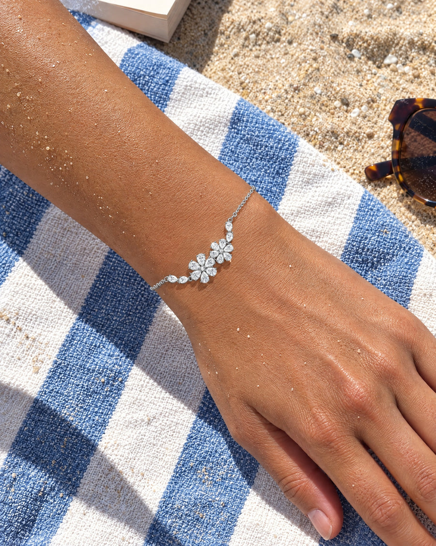 A forearm resting on a striped beach towel in bright sun, the floral bracelet on the wrist.