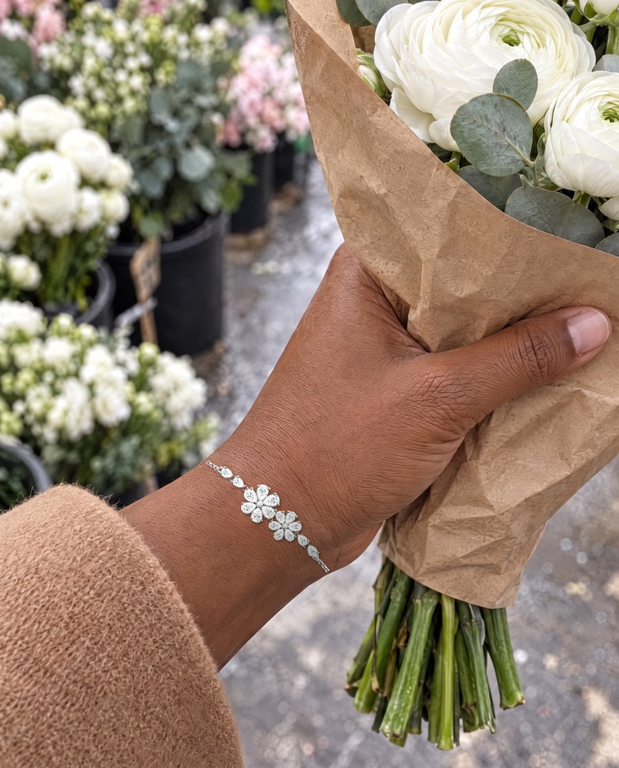 A hand holding a paper-wrapped bunch of white ranunculus at a flower market, the floral bracelet on the wrist.
