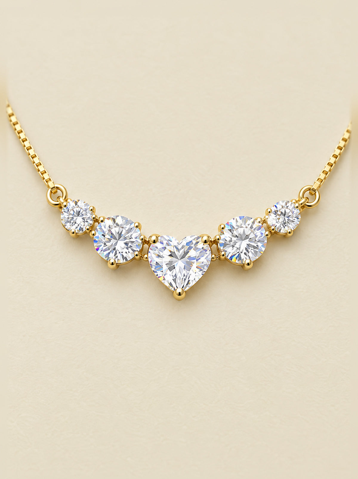 Close view of the five-stone bar: a heart-cut moissanite at the center held in prongs, a round brilliant on each side and a smaller one at each end, light breaking into color at the facets, gold-plated sterling silver.