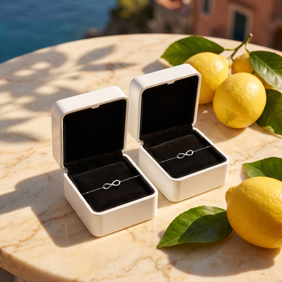 Two open white boxes (black velvet inside) on a sunlit marble table with lemons and leaf shadows.
