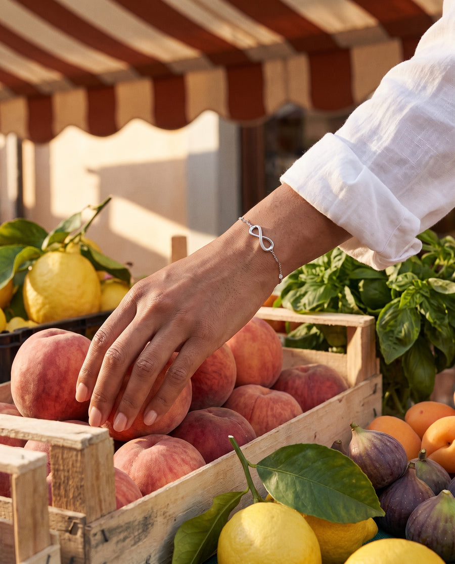 A summer market: her hand choosing ripe peaches from a wooden crate, warm sun, colourful produce.