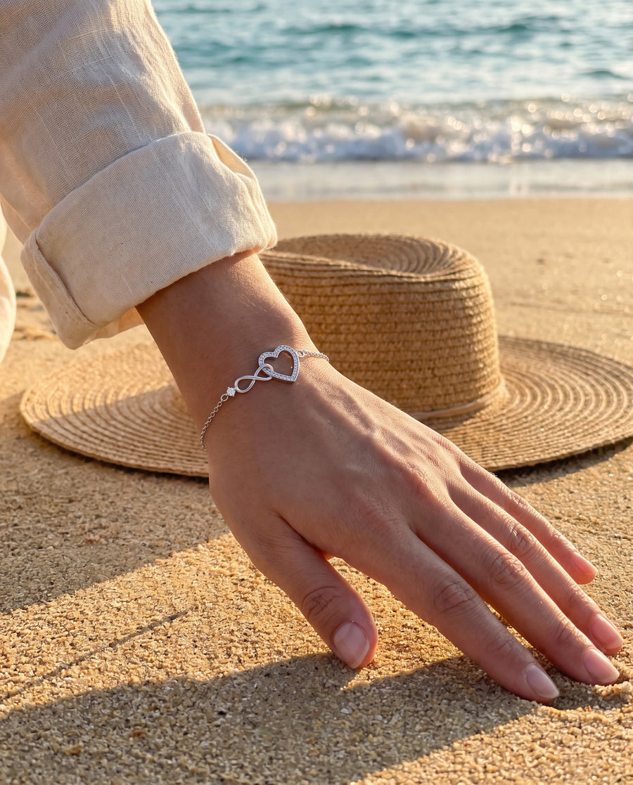 A Mediterranean beach at golden hour: her hand resting on warm sand beside a straw hat, soft shadows.