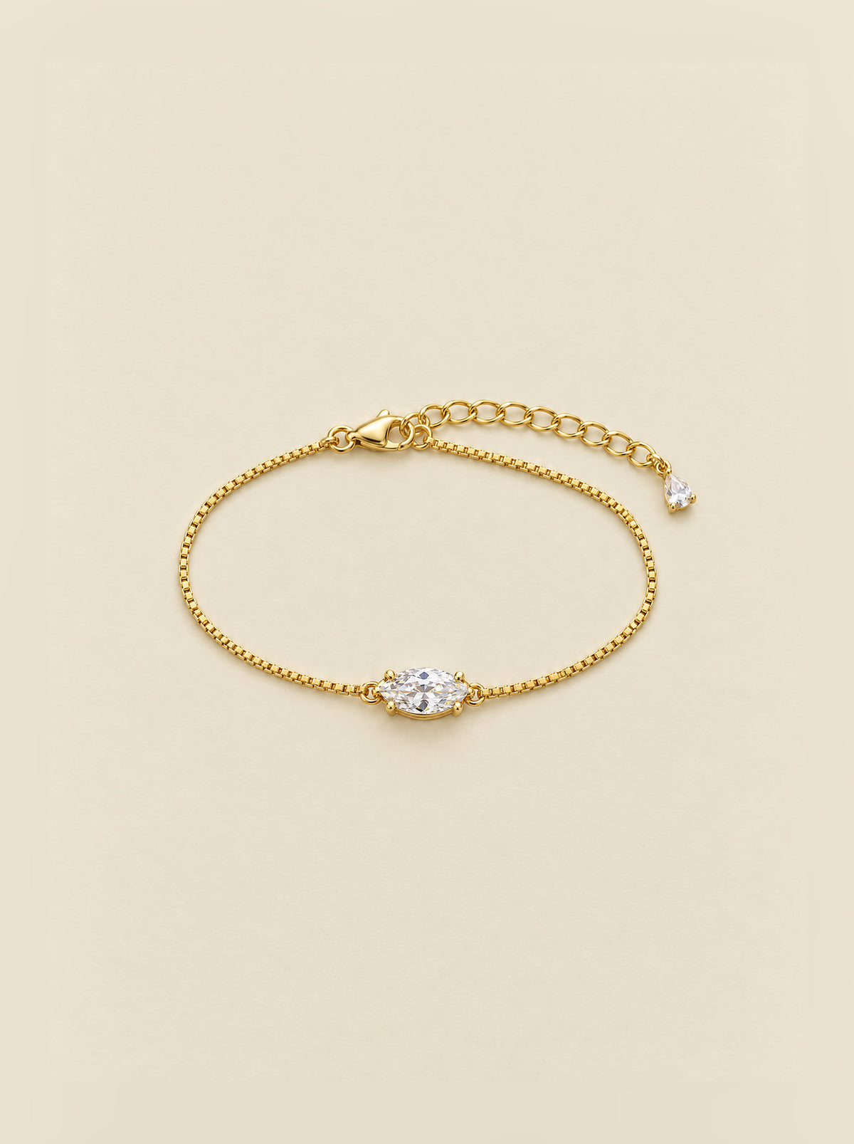 The Mossante Marquise Bracelet laid on a warm cream ground: a fine box chain in gold plated sterling silver, a single marquise moissanite set east-west at the center, a lobster clasp and an extension chain ending in a tiny pear-shaped drop.