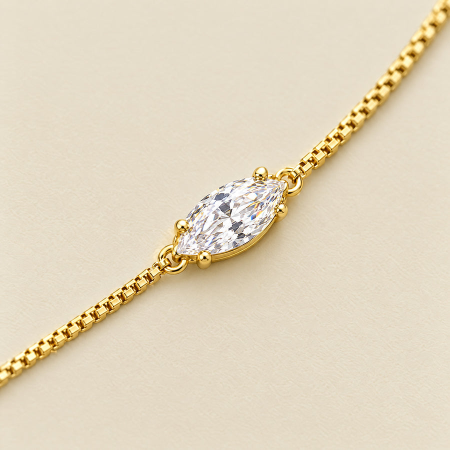 Close view of the marquise moissanite in its four-prong basket on the box chain, on a cream ground.