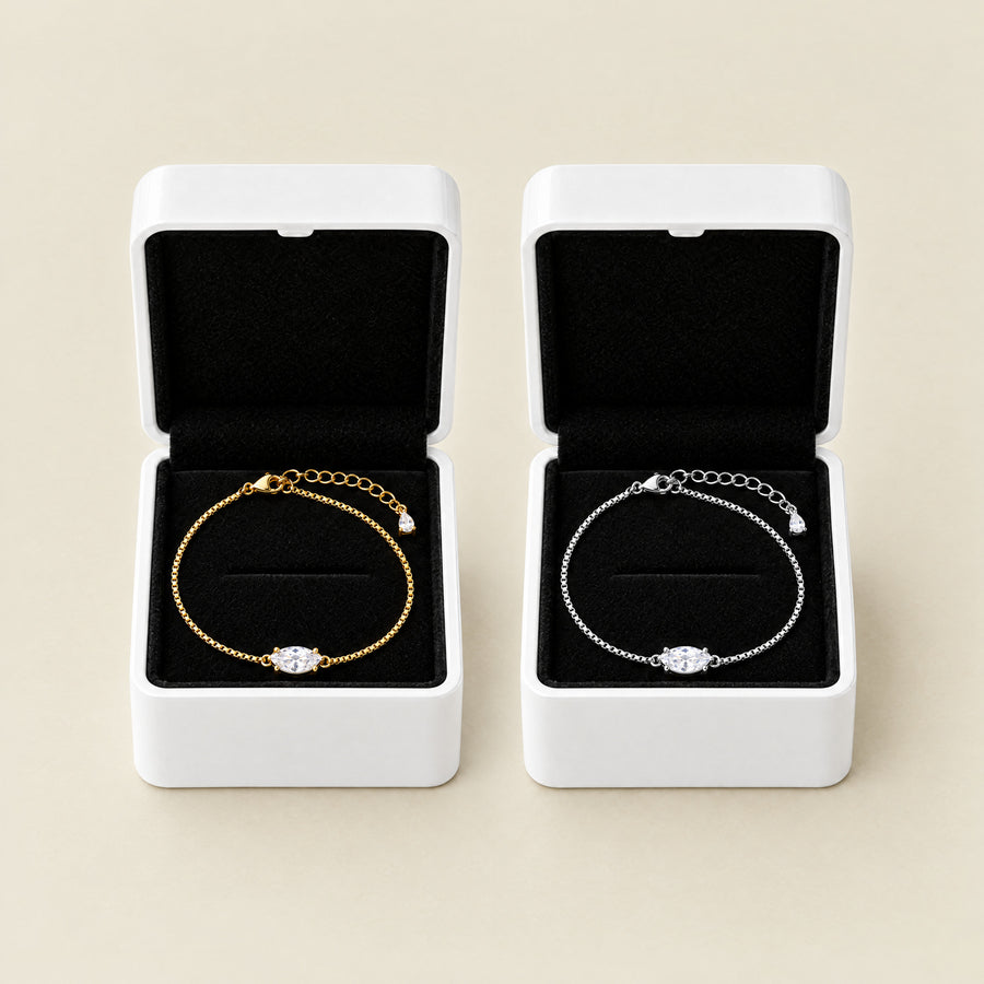 Two marquise bracelets side by side on a cream ground, each in its own open white box with a black velvet interior, one gold plated and one silver.