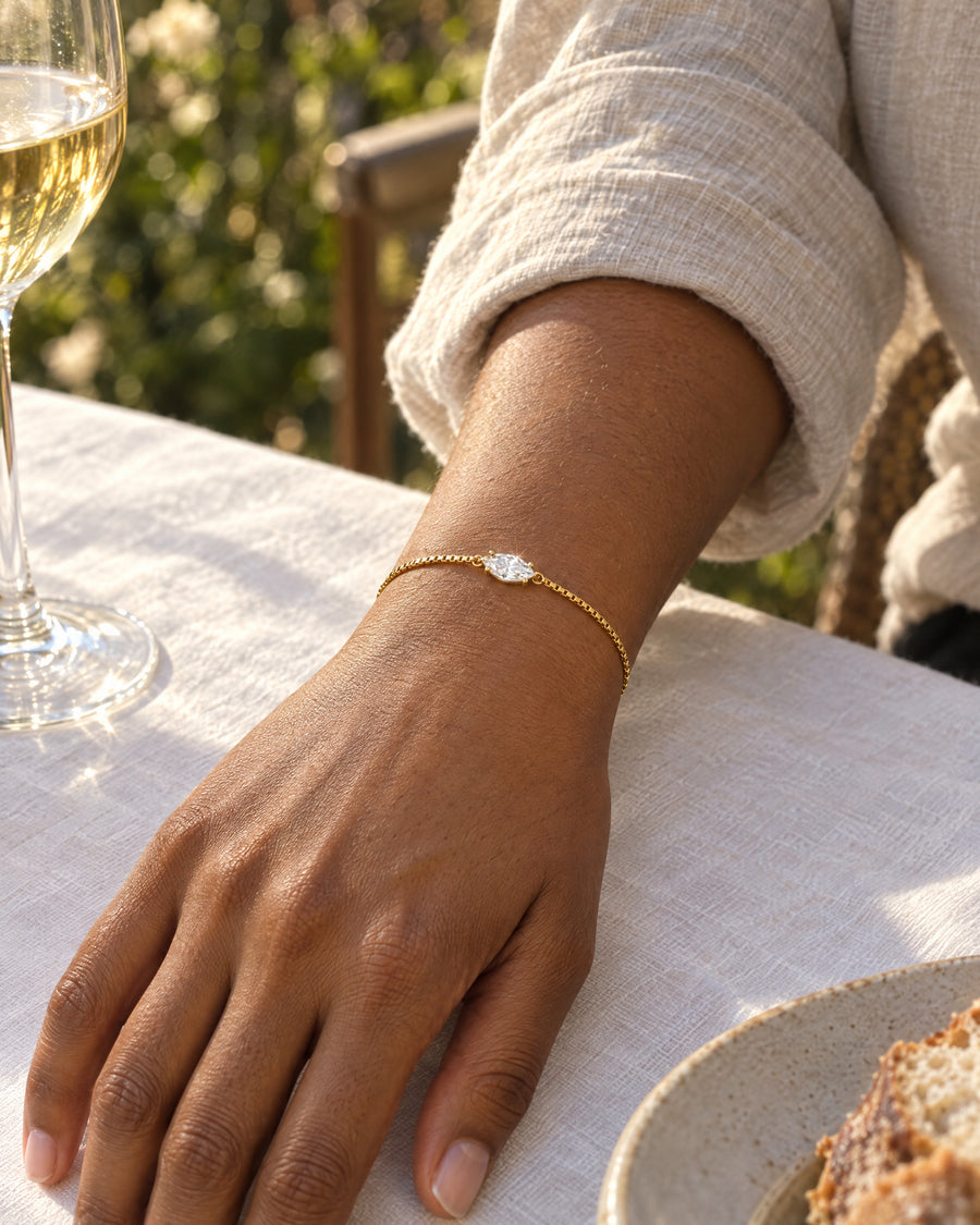 A Black woman's wrist resting on a white linen tablecloth beside a glass of white wine in late afternoon sun, the marquise stone lying along the top of the wrist.