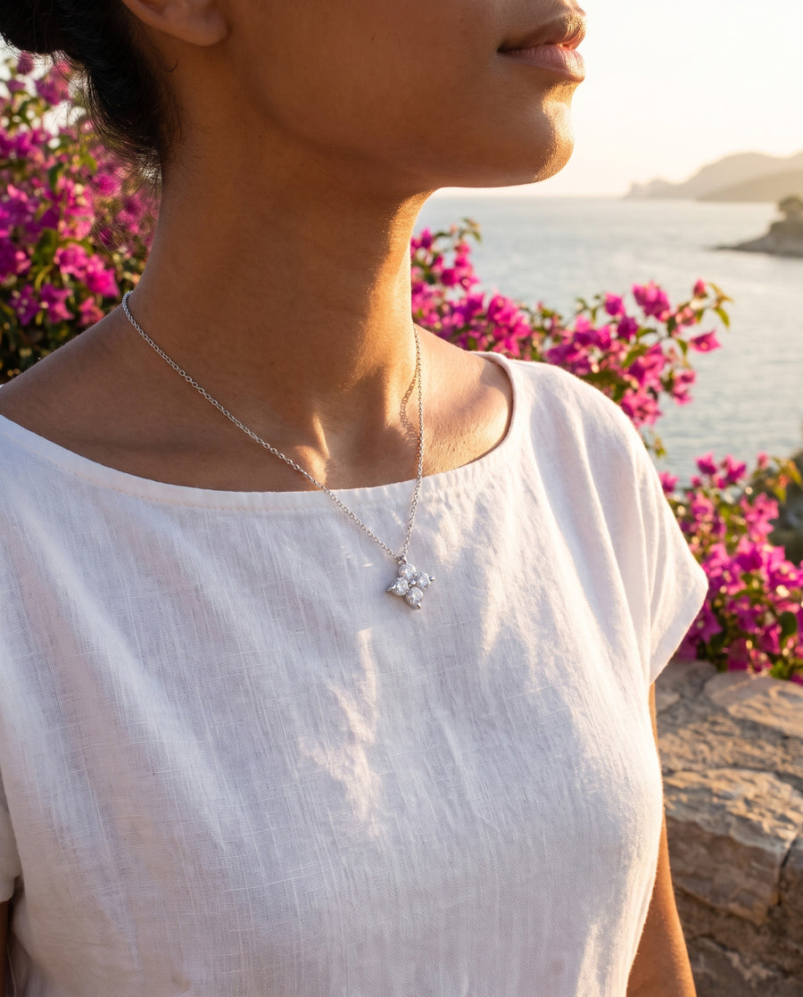 A sunlit terrace above the sea at golden hour, an open white linen shirt, wind in her hair, cropped at the chin.