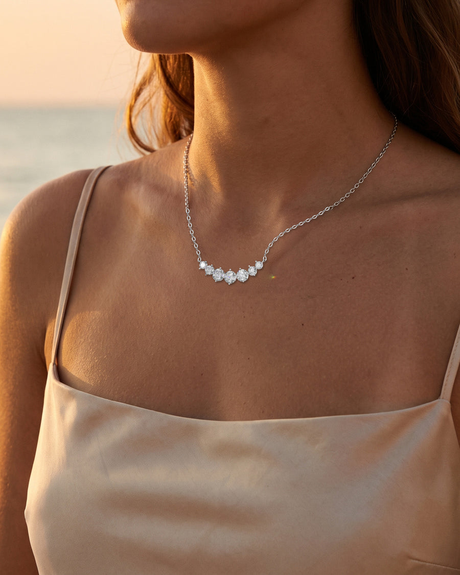 A Mediterranean beach at sunset in a simple silk slip dress, the sea behind, cropped at the chin.