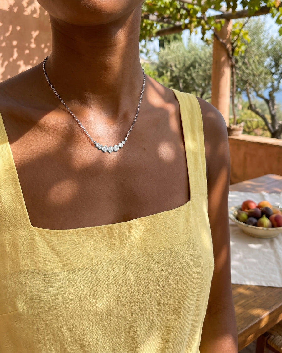 A garden lunch under a vine pergola in a square-neck sundress, dappled light, cropped at the chin.