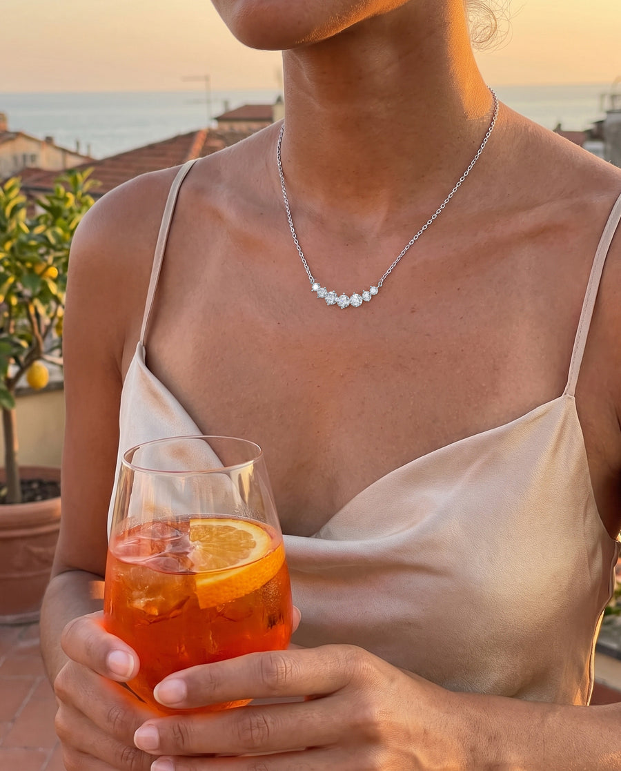 Aperitivo on a rooftop at sunset in a satin slip dress, a glass of spritz held low, cropped at the chin.