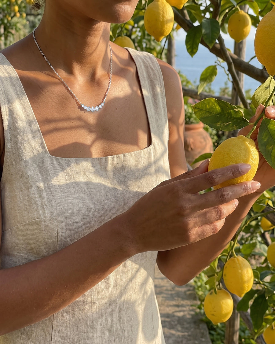 A lemon-garden walk in a linen sundress, warm sun and leaf shadows on her skin, cropped at the chin.