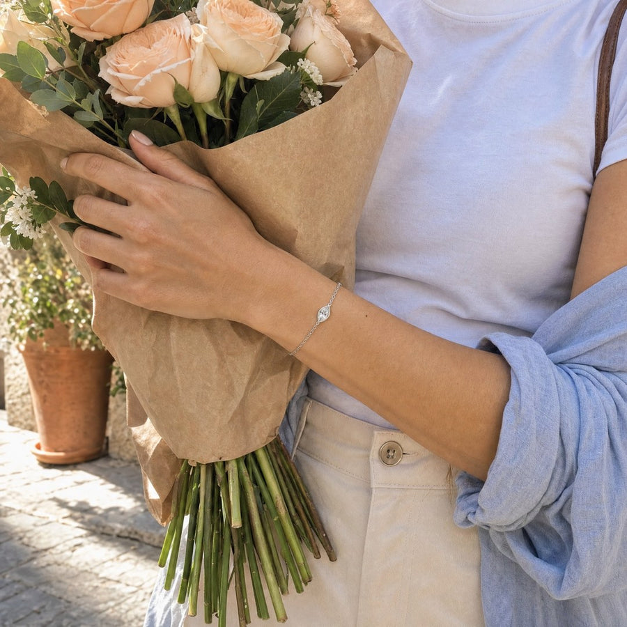 Hands holding a bouquet of roses in kraft paper outside a flower shop, the silver marquise-cut bracelet at the wrist.
