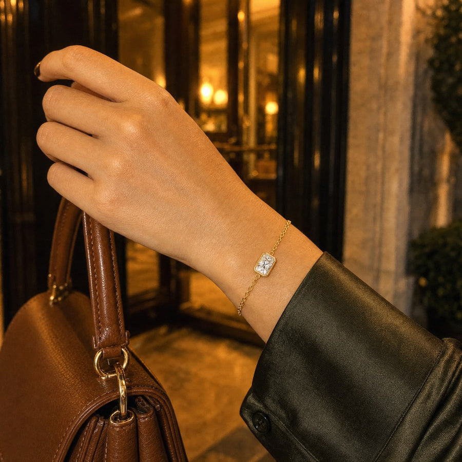 A hand on the strap of a leather bag, olive satin shirt, the gold plated radiant-cut bracelet at the wrist.