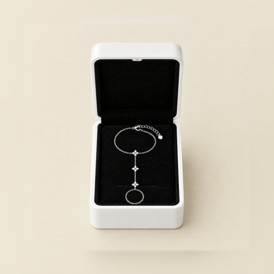 The hand chain in its open white box, black velvet inside, the lid up, on a cream ground.