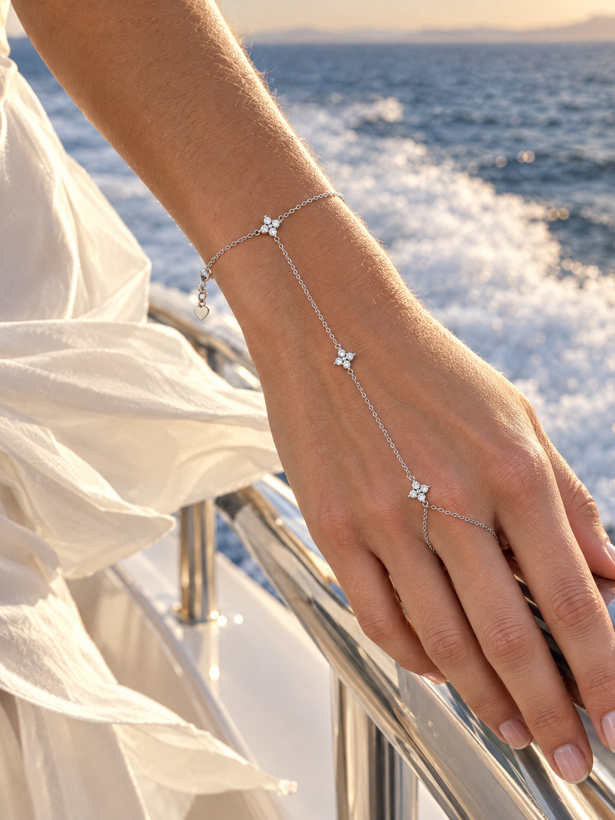 The hand chain on a hand at a yacht rail with the wake behind, white silk at the wrist.