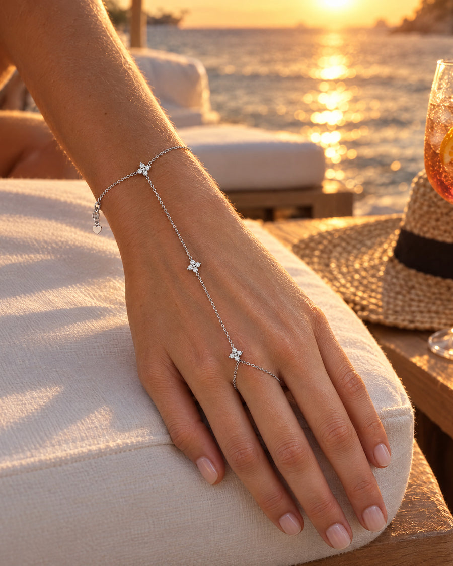 A woman's hand at a beach club at sunset, the chain warm against the light.