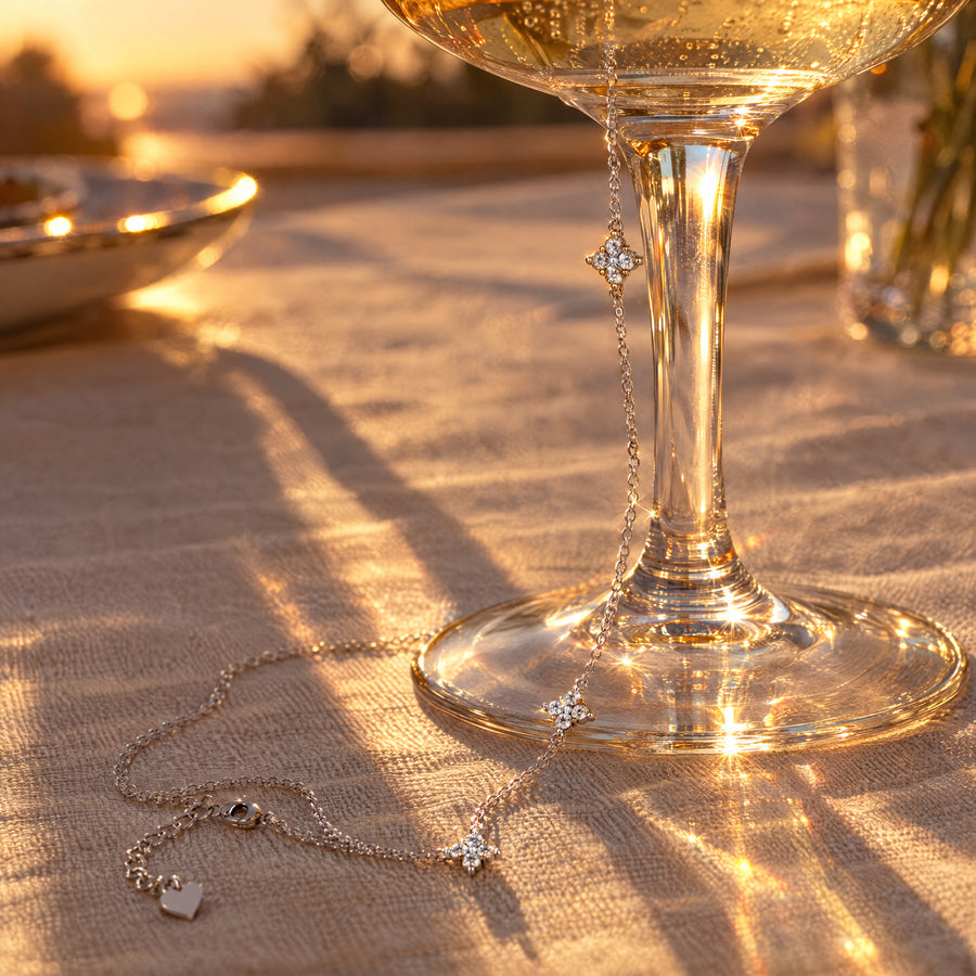 The hand chain laid at the foot of a champagne coupe at sunset, all three stars along the chain.