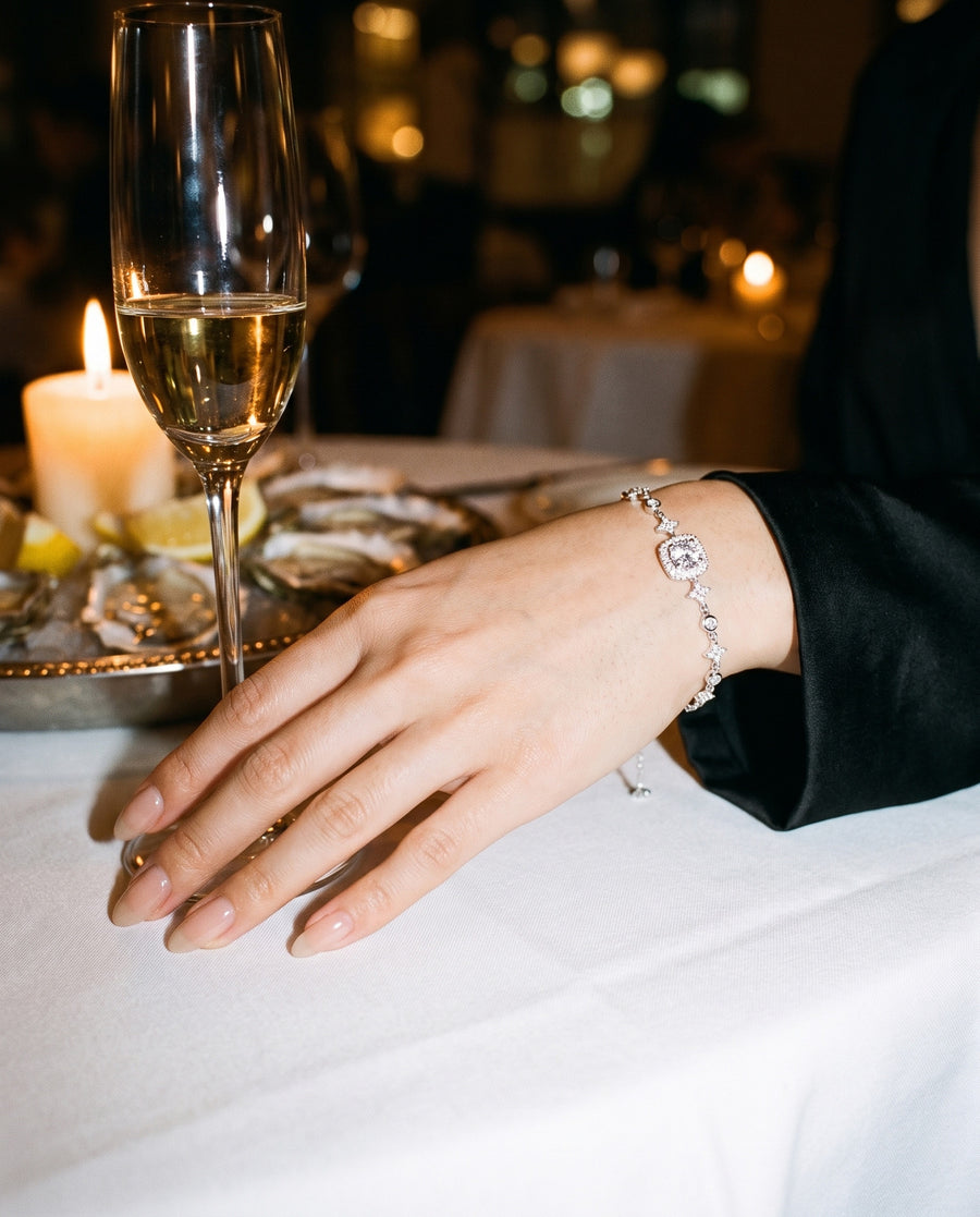 An upscale restaurant at night: candlelight, her hand beside a glass of champagne and oysters on white linen.