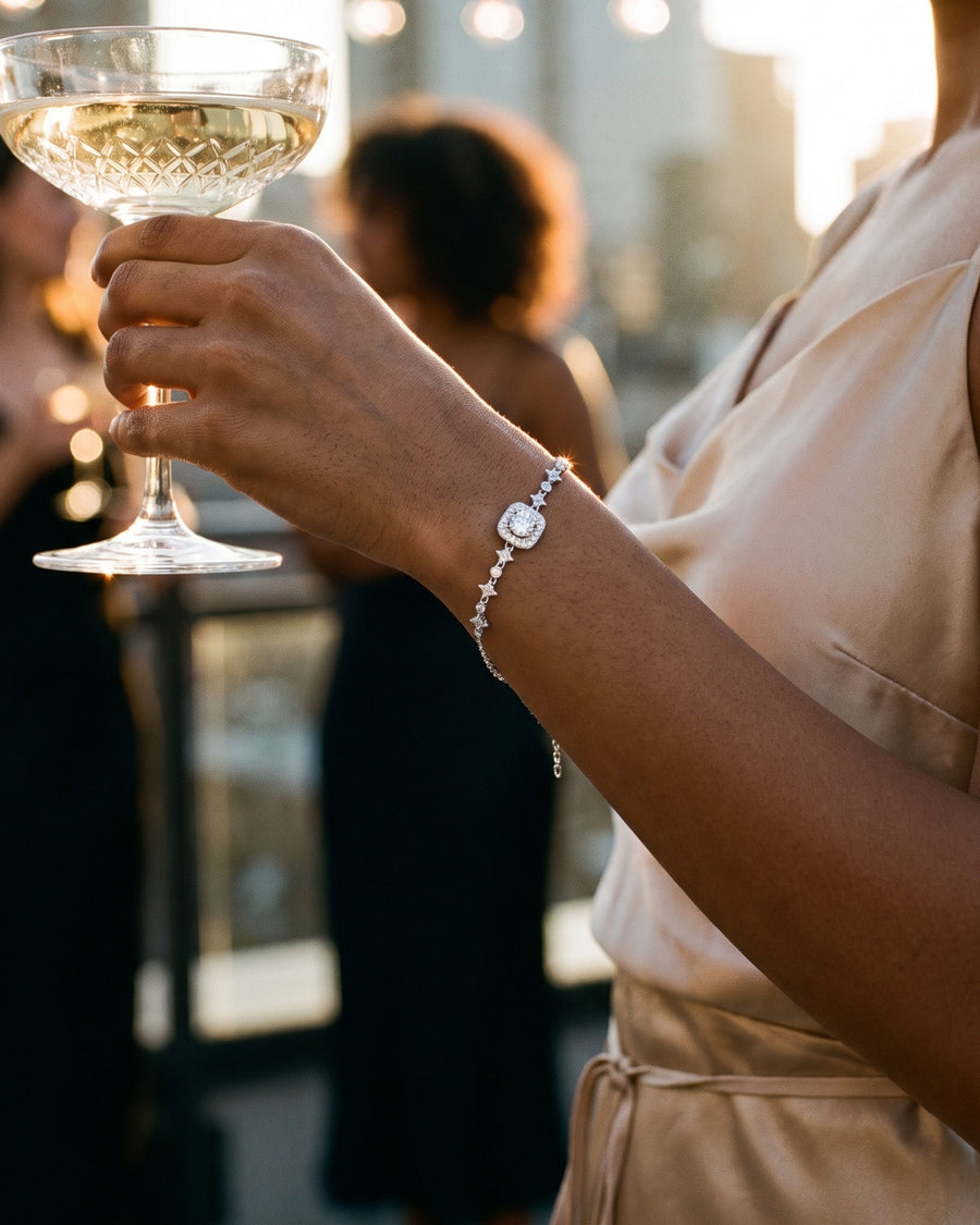A rooftop party at golden hour: her hand raising a coupe of champagne, friends softly blurred behind.