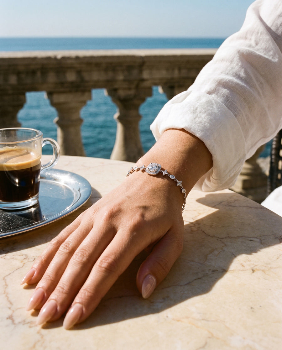 A private terrace at a luxury hotel: her hand on a marble table beside an espresso and a silver tray, sea view.