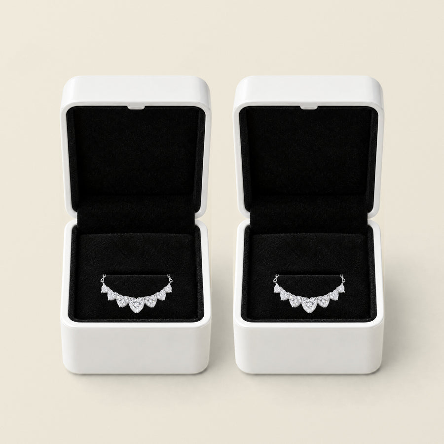 Two open white boxes side by side on a cream ground, black velvet inside each, a silver sweetheart necklace in each with its seven hearts resting on the velvet pad.