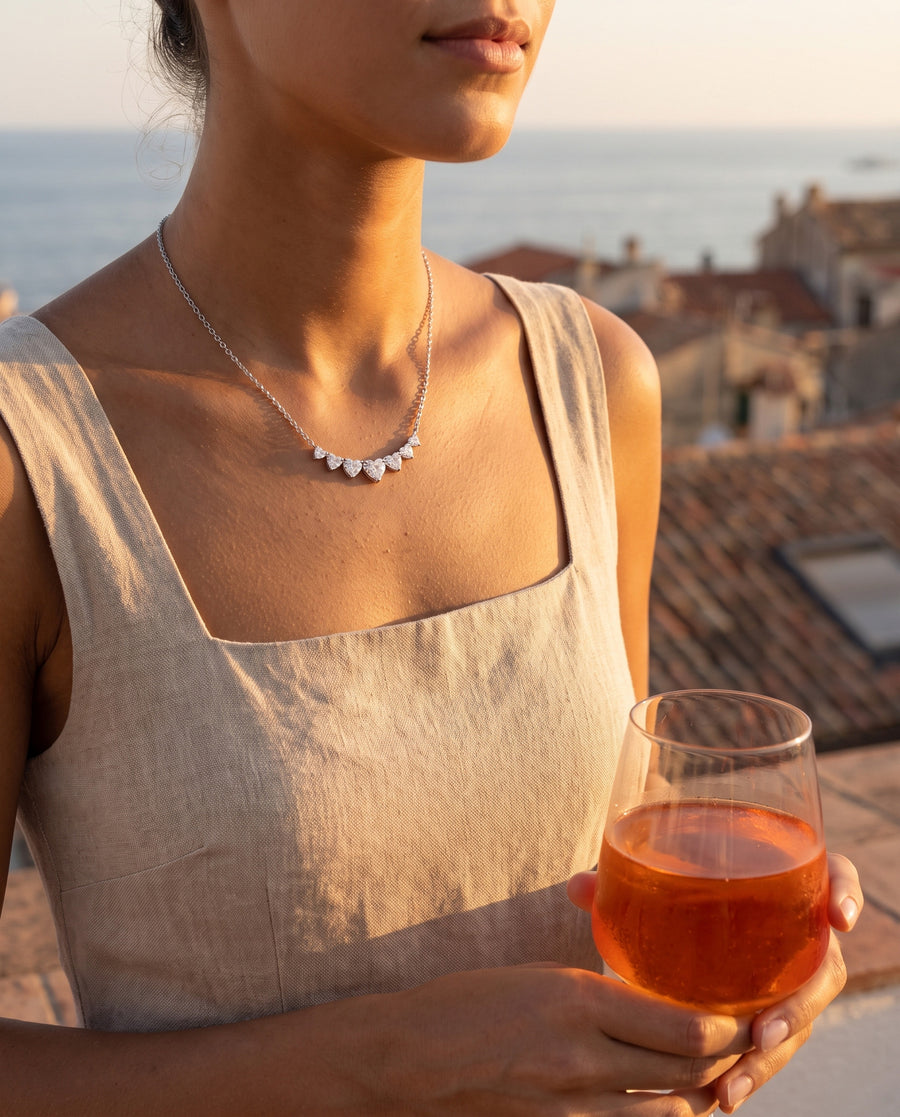 Aperitivo on a rooftop at sunset in a satin slip dress, a glass of spritz held low, cropped at the chin.