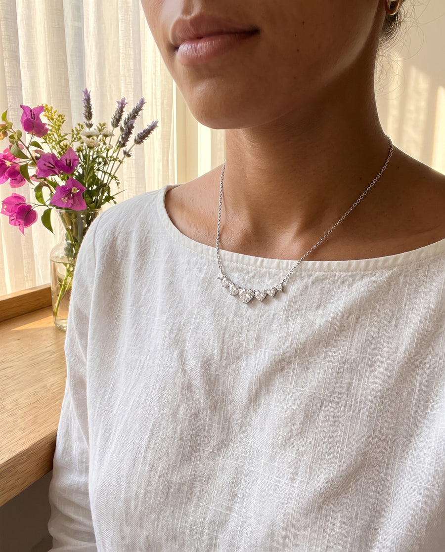 A sunlit morning room with sheer curtains in a white cotton camisole, soft warm light, cropped at the chin.