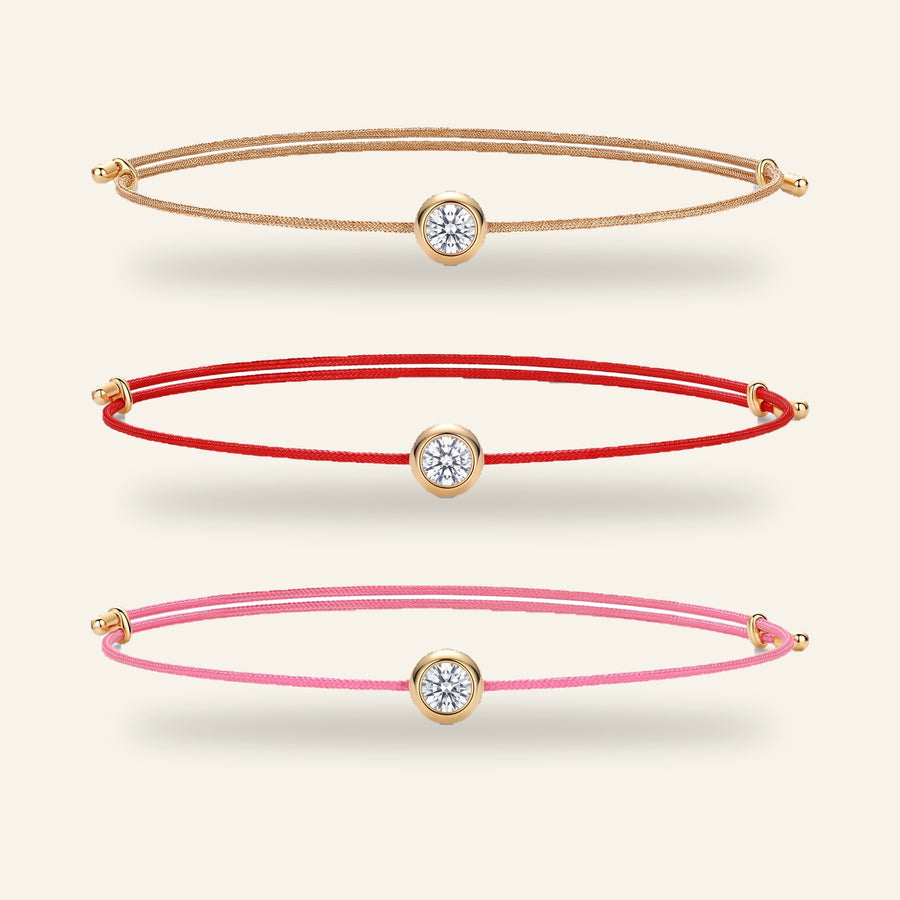 Three Mossante cord bracelets in Gold, Red and Pink laid one above the other